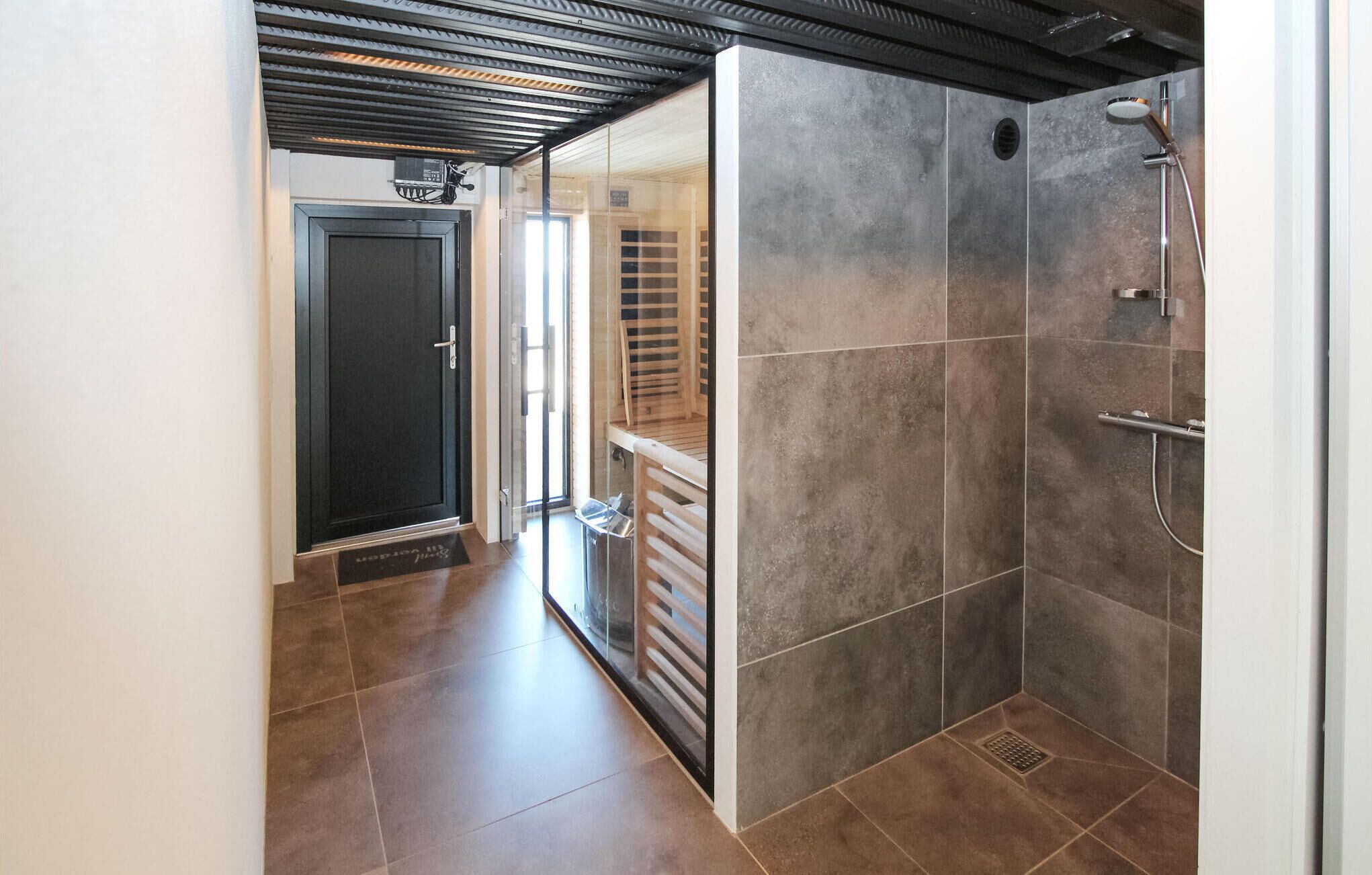 Un baño moderno con ducha, paredes de azulejos y una puerta que da a otra habitación.