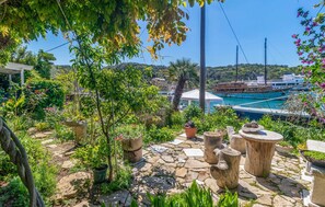 Stroll through the serene garden, surrounded by lush potted plants and rustic seating areas, with a tranquil marina view.