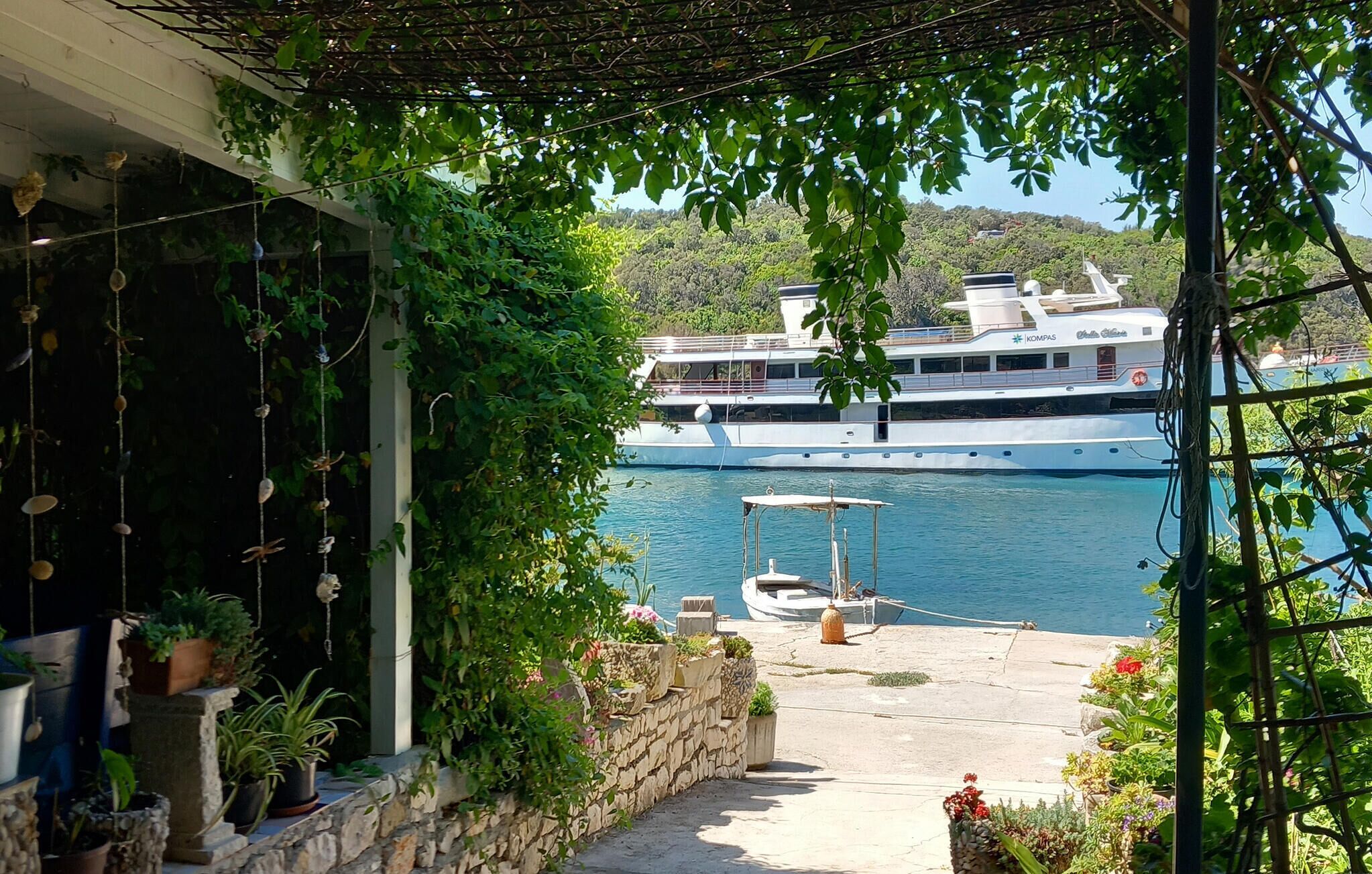 A boat docked at a marina with a stone pathway leading to a covered area with potted plants.