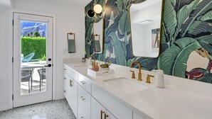 Un baño con tocador blanco, dos lavamanos, grifos dorados y un espejo grande.