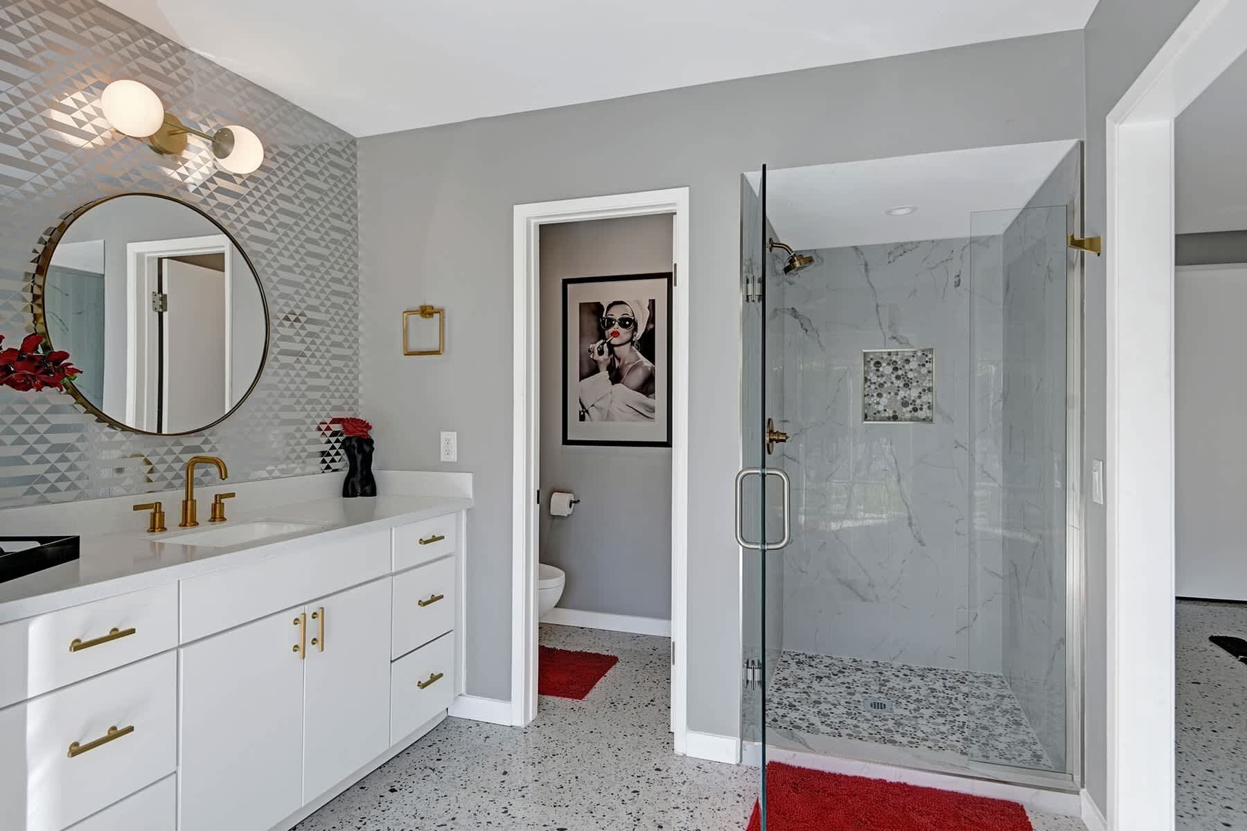 Une salle de bain moderne avec un meuble-lavabo blanc, un grand miroir, une douche à portes en verre et un mur orné d’un motif.