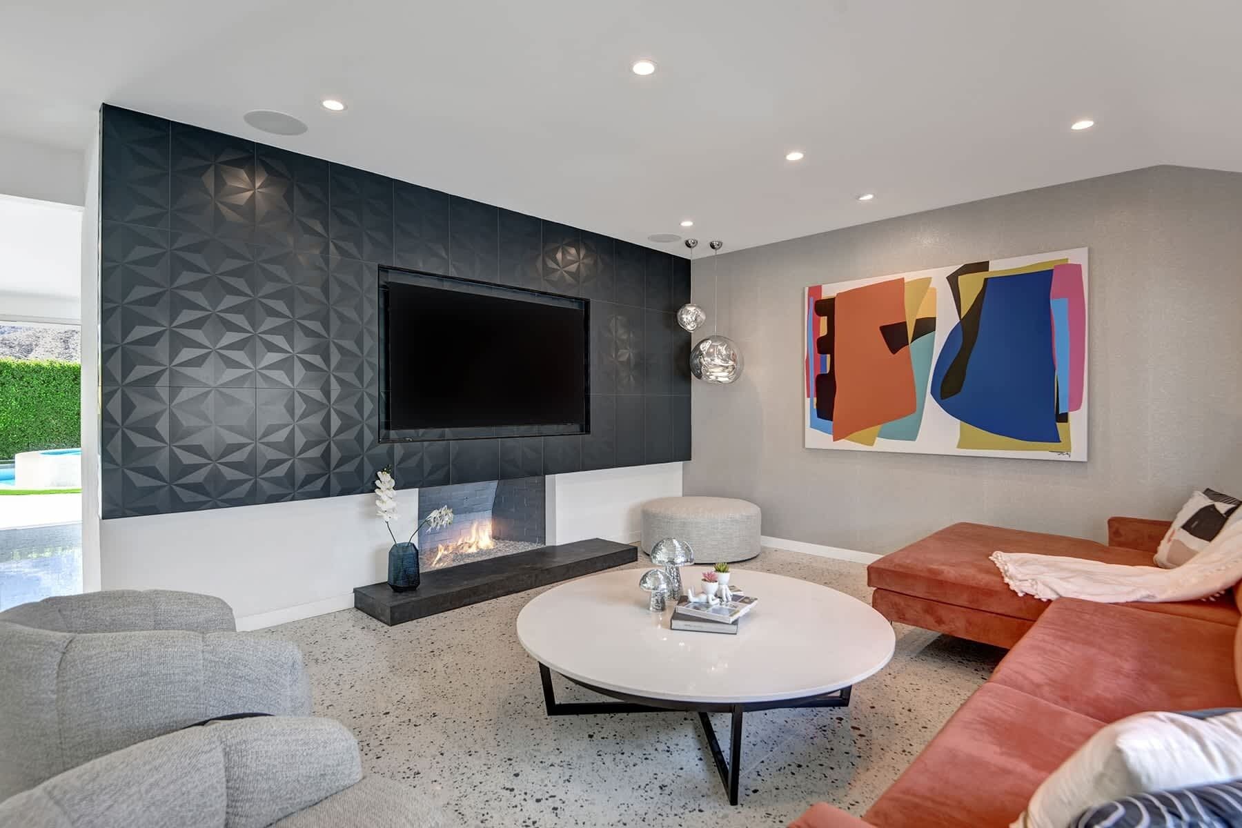 A modern living room with a flat-screen TV, a fireplace, a round coffee table, and a colorful abstract painting.