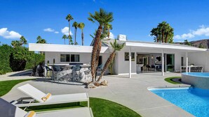 Una casa moderna con piscina, mobiliario de exterior y palmeras.