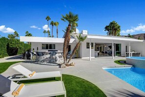 A modern house with a pool, outdoor seating, and palm trees.