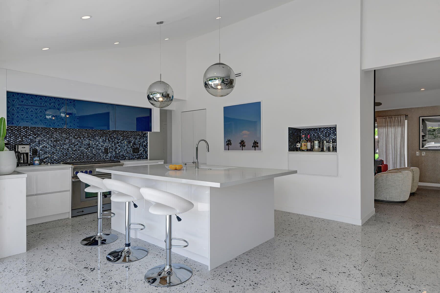 A modern kitchen with a central island, bar stools, a coffee machine, and decorative wall art.
