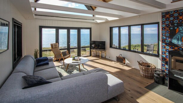 A modern living room with a large sofa, a coffee table, and a TV. There are large windows offering a view of the sea. - Gorgeous home in Samsø with sauna (Samsø)