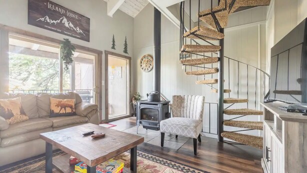 Una sala de estar acogedora con un sofá, una mesita de centro y una chimenea. Una escalera de caracol conduce a un nivel superior.