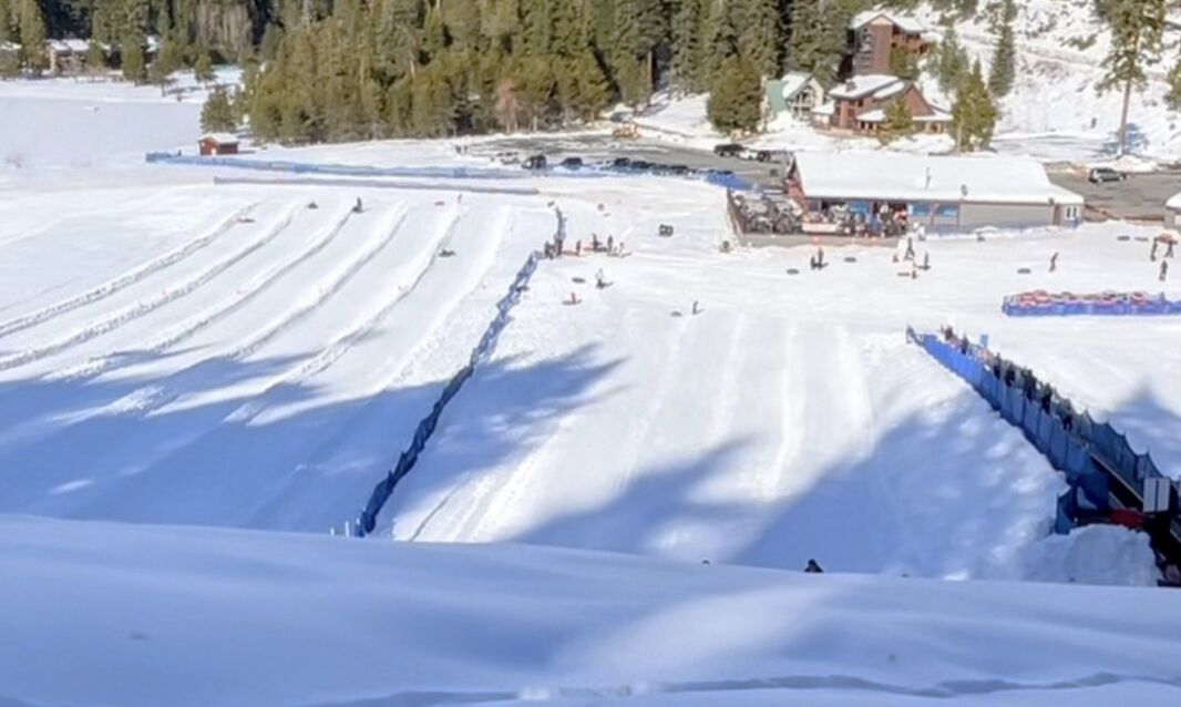 A snow-covered ski slope with marked trails and a lodge in the background.