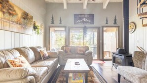 Una sala de estar acogedora con dos sofás, una mesa de centro y una chimenea. Dos puertas dan acceso a un balcón con vistas a árboles.