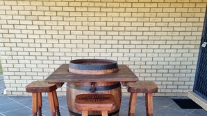 A wooden table and stools with a barrel centerpiece, set on a tiled patio against a brick wall. - BLK Stays Guest House Deluxe Back Units Morayfield (Morayfield)