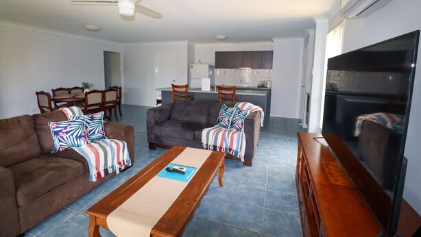 A living room with a sofa, coffee table, and TV. There is a kitchen in the background with a refrigerator and cabinets. - BLK Stays Guest House Deluxe Back Units Morayfield (Morayfield)