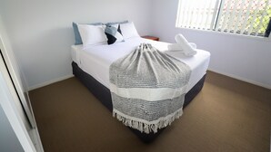 A neatly made bed with a white duvet, a grey and white crocheted throw, and a white towel on the footboard. - BLK Stays Guest House Deluxe Back Units Morayfield (Morayfield)