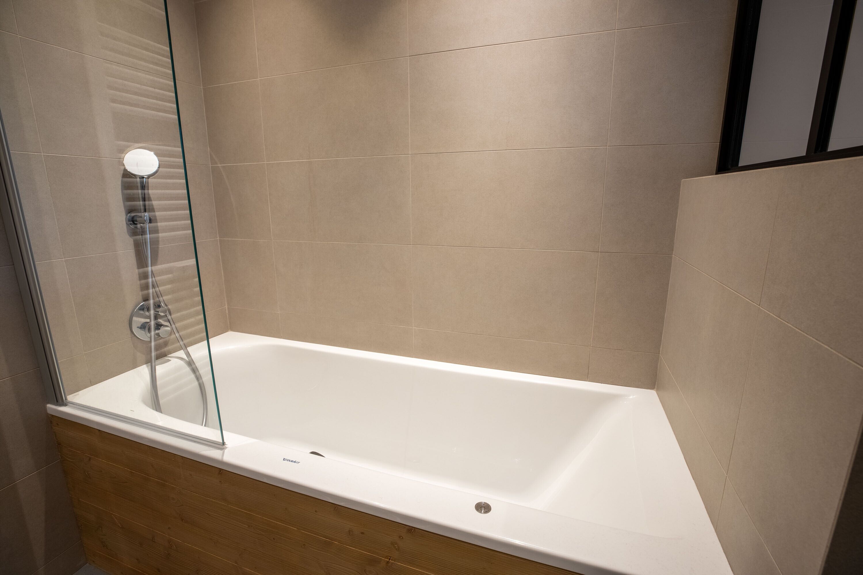 Une salle de bain moderne avec une douche à parois de verre, une baignoire blanche et un revêtement de sol en bois.