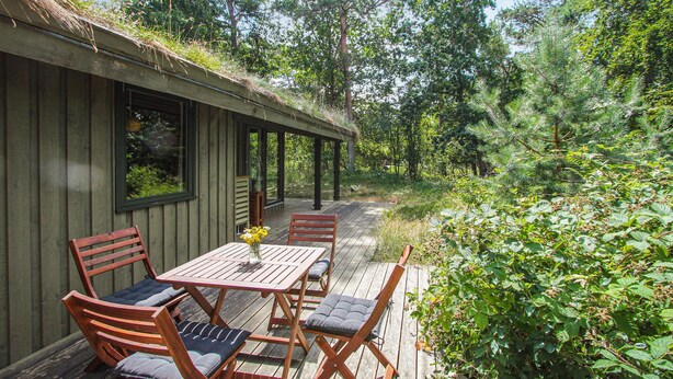 A wooden deck with a table and chairs, surrounded by lush greenery and trees. - Stunning home in Samsø with WiFi (Samsø)