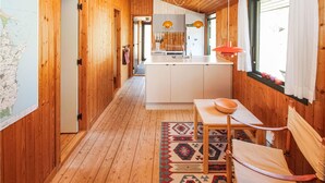 A narrow hallway with wooden walls and a wooden floor leading to a kitchen area with white cabinets and a central island. - Stunning home in Samsø with WiFi (Samsø)
