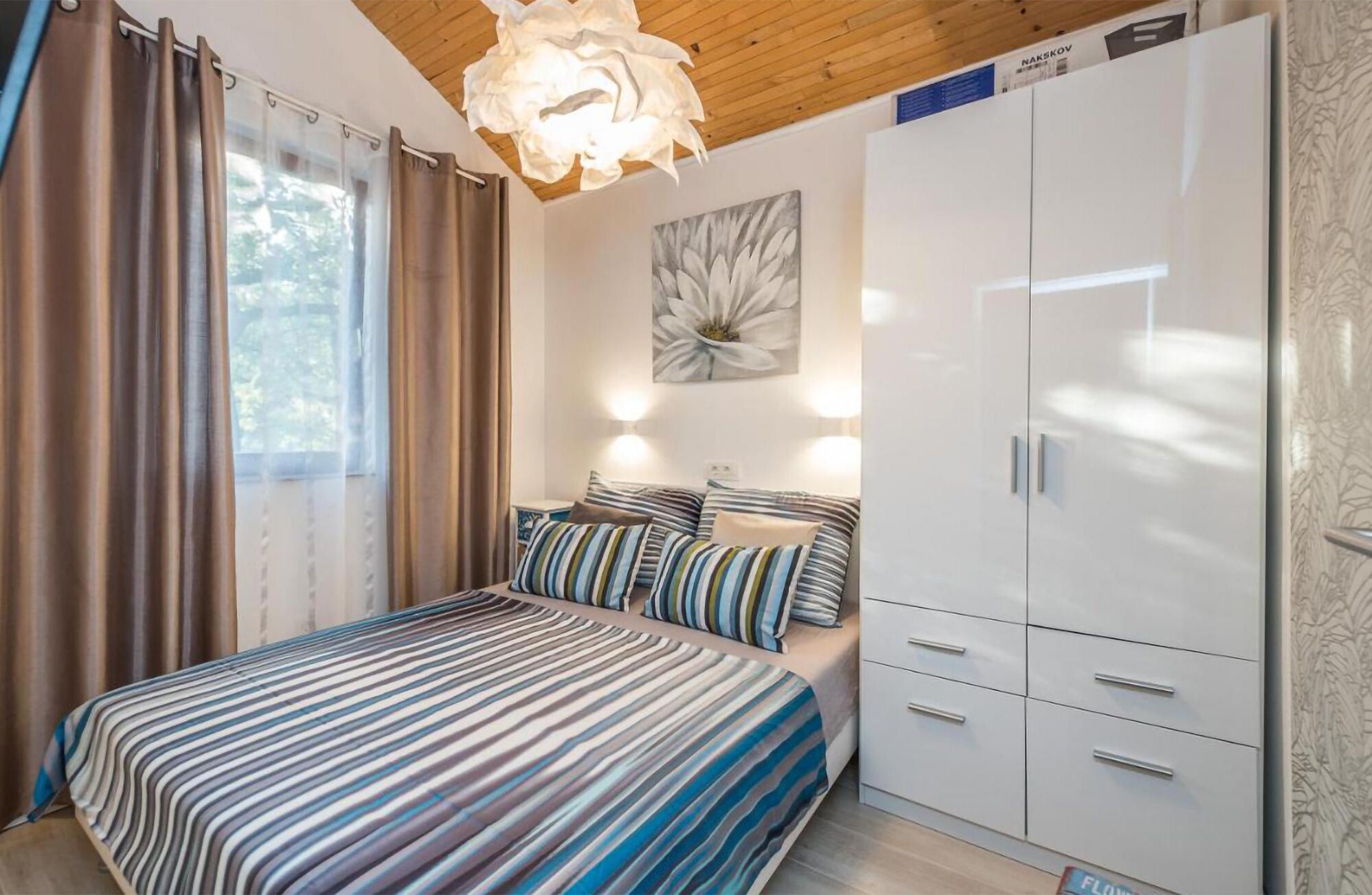 A bedroom with a bed, a wardrobe, a painting, and a light fixture.