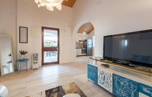 Relax in this stylish living room with a large flat-screen TV, comfortable seating area, and door leading to a balcony with outdoor views.