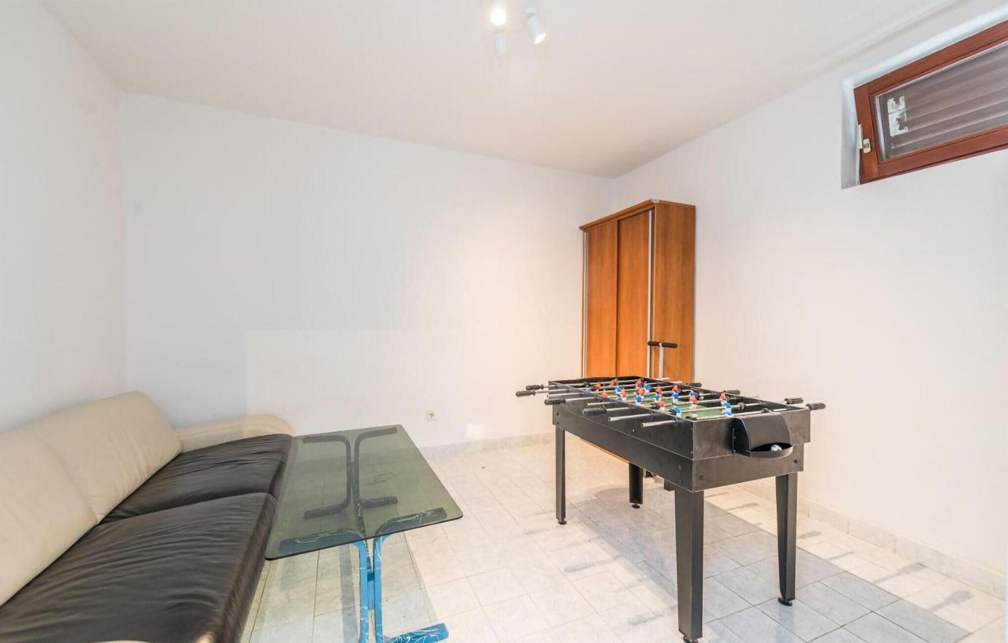 Quarto com sofá, mesa de centro de vidro e mesa de pebolim.
