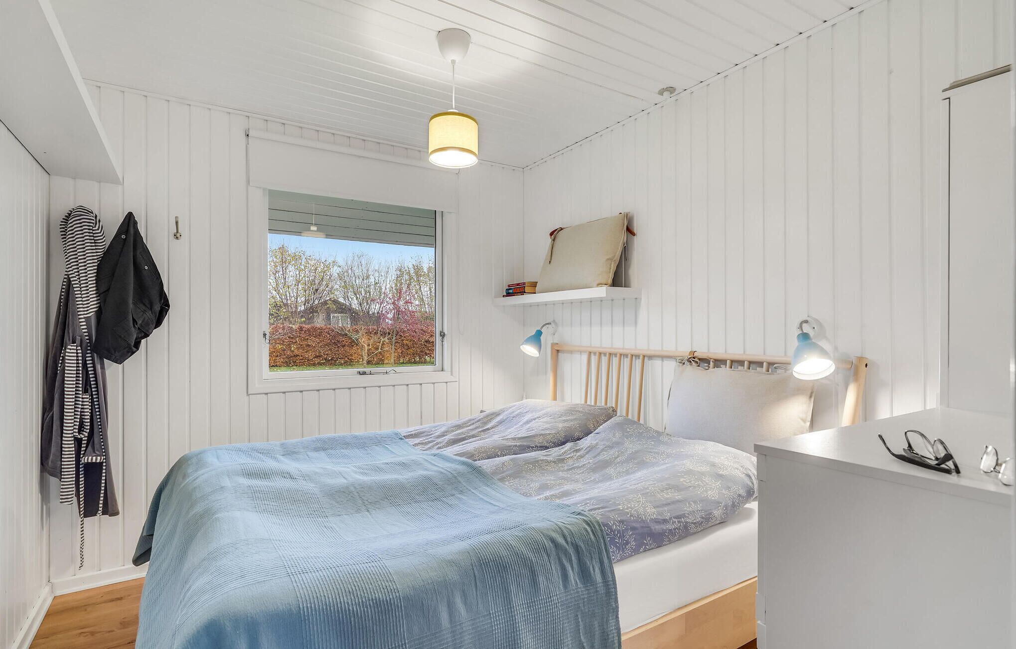 A bedroom with a bed, bedside lamps, a window, and a coat rack.