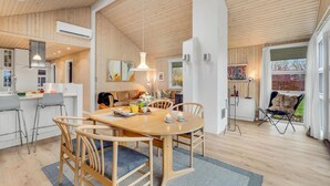 A modern kitchen with white cabinets, a dining area with a wooden table and chairs, and a cozy living space with a sofa and a dog. - Beautiful home in Haarby with WiFi (Haarby)