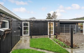 Ein modernes Gebäude mit dunkler Fassade, einem Glastür-Eingang und einem kleinen Gartenbereich mit Gras und Pflanzen.
