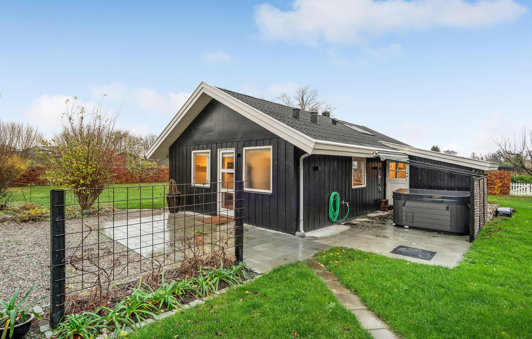 A modern house with a dark exterior, a garage, and a hot tub in the backyard.