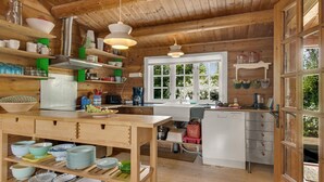 Eine rustikale Küche mit Holzböden, Regalen und einer Kochinsel, durch ein Fenster fällt natürliches Licht.