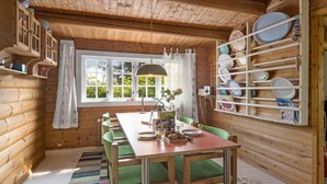 Ein Holzblockhaus-Interieur mit Esstisch, Stühlen, einem Fenster mit Vorhängen und einem an der Wand befestigten Geschirrhalter.