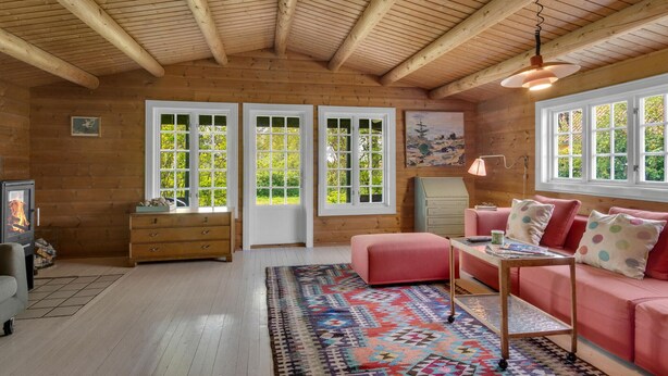 Ein gemütliches Blockhaus-Interieur mit Holzwänden, einem rosa Sofa, einem gemusterten Teppich und einem Kamin.