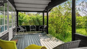 Ein überdachter Außenbereich mit Holzterrasse, zwei Korbstühlen und einem gelben Stuhl.