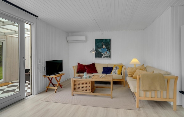 Ett modernt vardagsrum med en soffa, ett soffbord, en tv på ett tv-bord och en tavla på väggen.