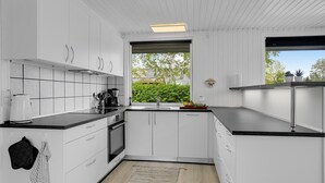A modern kitchen with white cabinets, black countertops, and a large window offering a view of greenery.