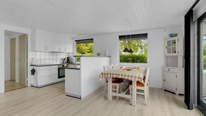 A compact kitchen with white cabinetry, a dining table with a checkered tablecloth, and a view of greenery through the windows.