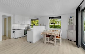 Modern kitchen with oven and dining area for four, offering a view of lush greenery.