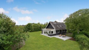 A modern house with a large glass extension, surrounded by lush greenery.