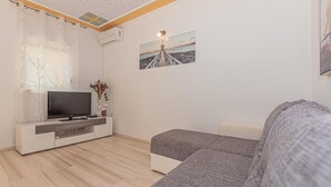 Un salon moderne avec un téléviseur à écran plat, un meuble de rangement blanc, un canapé gris et un tableau représentant un phare accroché au mur.