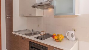 Une cuisine moderne dotée d’un évier en acier inoxydable, d’une cuisinière encastrée et d’une hotte aspirante. On peut voir un panier de fruits contenant des oranges et des bananes sur le comptoir.