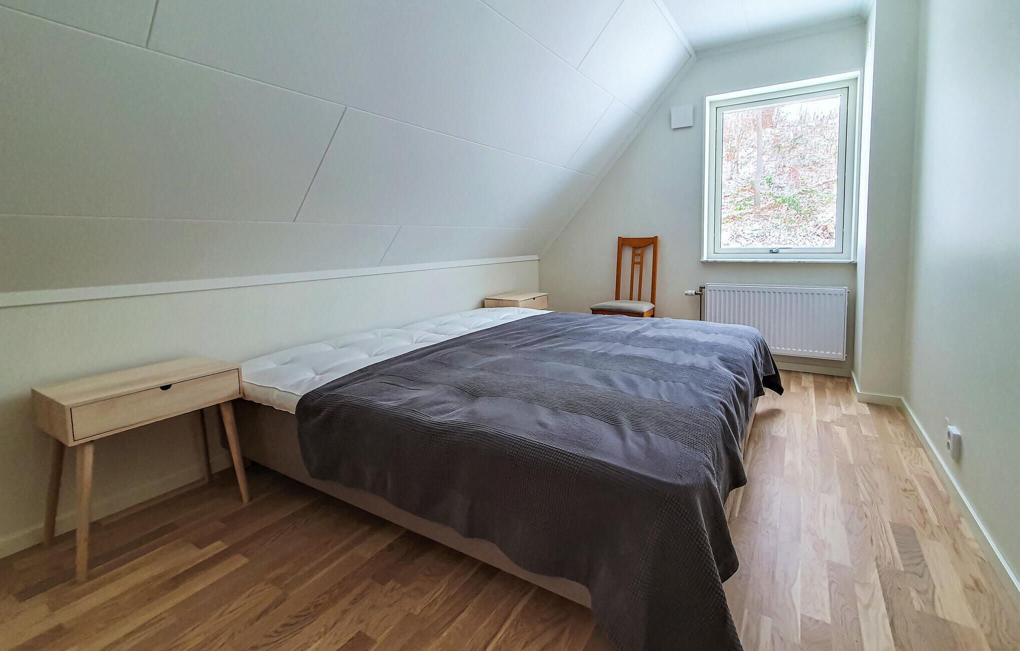 Ein Schlafzimmer mit einem Bett, einem Nachttisch, einem Holzhocker, einem Fenster und einer Heizung.