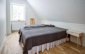 A bedroom with a sloped ceiling, a bed with a dark cover, a bedside table, and a chair. - Stunning home in Båstad with WiFi (Båstad)