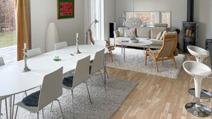 A modern living room with a dining area, a fireplace, and a large window with a view of trees. - Stunning home in Båstad with WiFi (Båstad)