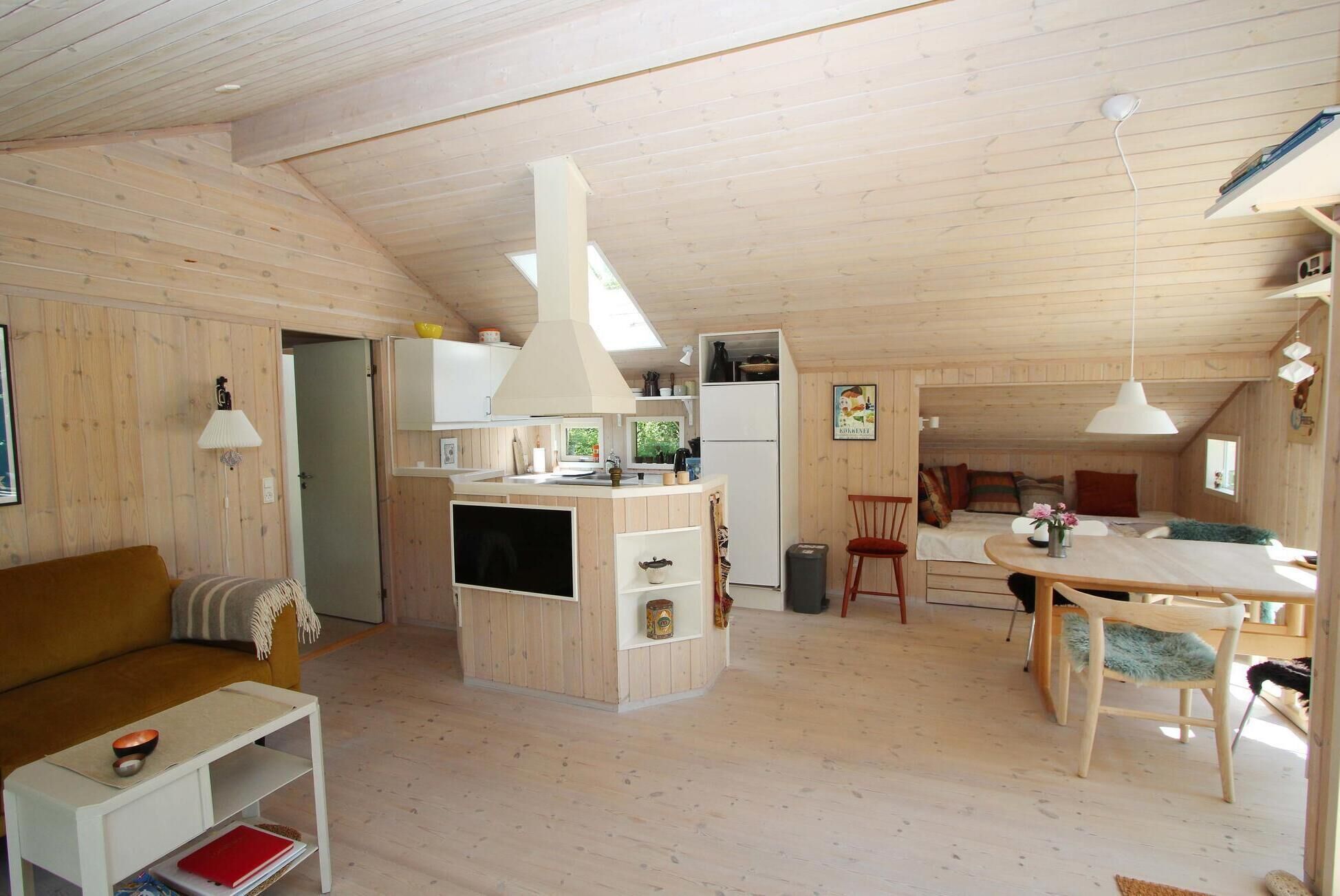 Interior acogedor de una cabaña con detalles de madera, una kitchenette, un comedor y una sala de estar con sofá y mesa.