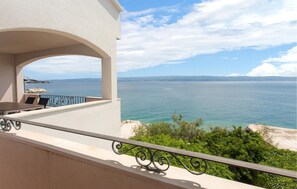 Uma varanda com vista para o mar, uma mesa com cadeiras e um corrimão.