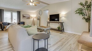 A living room with a sofa, a round table, a television, and a ceiling fan. - Peaceful Louisiana Escape: Fire Pit + Yard! (Covington)