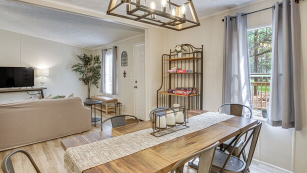 A dining area with a wooden table, metal chairs, a chandelier, and a view of the outdoors through a window. - Peaceful Louisiana Escape: Fire Pit + Yard! (Covington)