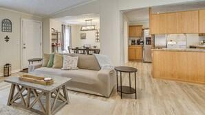 A living room with a sofa, coffee table, and kitchen area with wooden cabinets and appliances. - Peaceful Louisiana Escape: Fire Pit + Yard! (Covington)