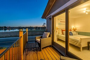 Un balcon avec une chaise en osier et une petite table, d’où l’on peut admirer un plan d’eau et un paysage lointain.