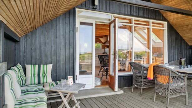 A cozy outdoor seating area with a wooden deck, a sofa with striped cushions, and wicker chairs. - Nice home in Kalundborg with WiFi (Kalundborg)
