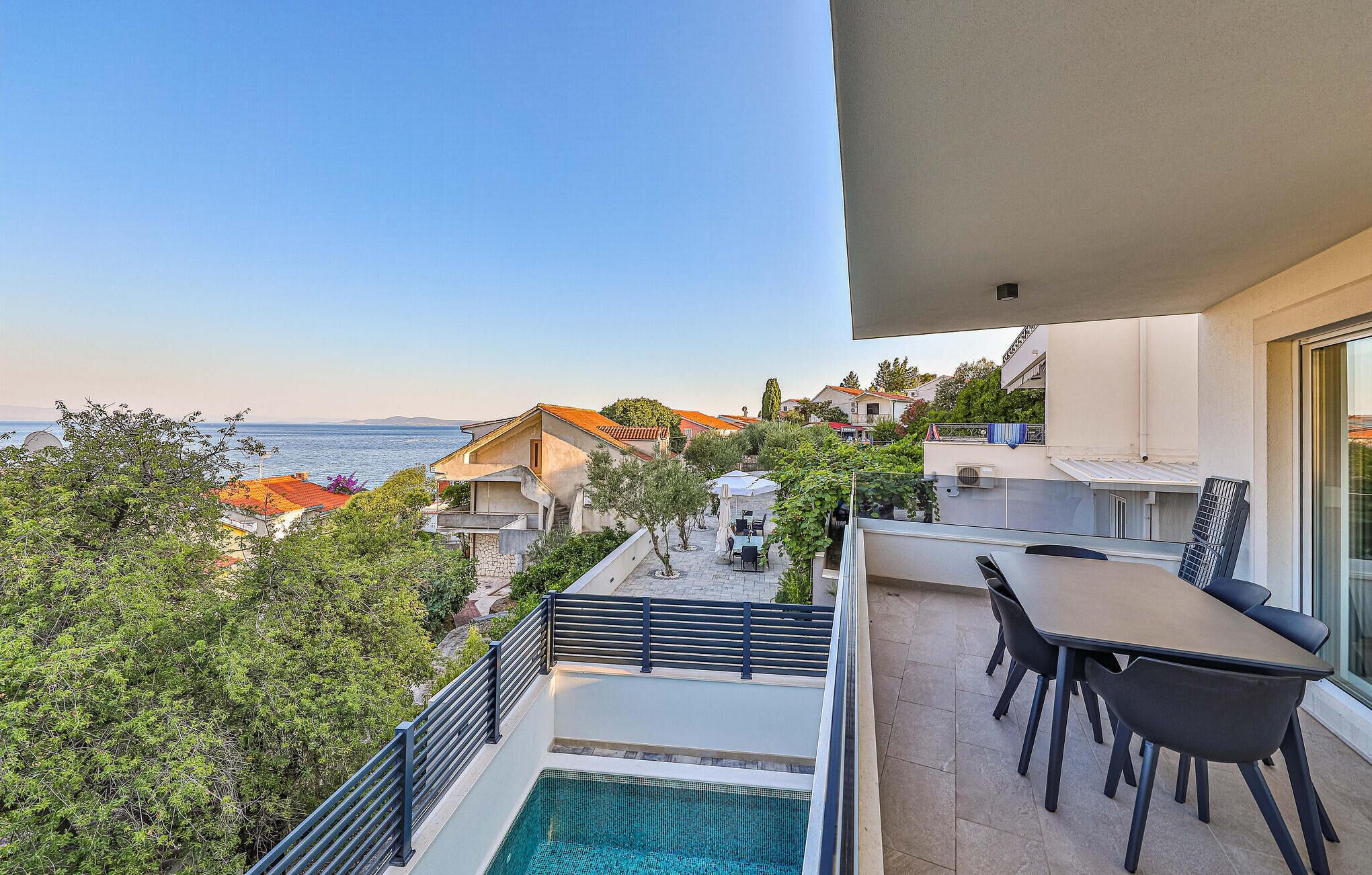 A balcony with a pool, outdoor seating, and a view of the sea and buildings.