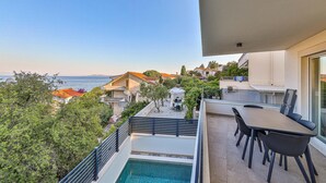 Un balcón con piscina, mobiliario exterior y vistas al mar y edificios.