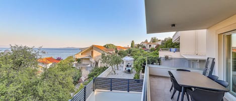 Een balkon met zwembad, buitenmeubilair en uitzicht op zee en gebouwen.